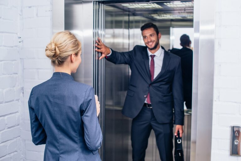 smiling handsome businessman holding elevator door for woman