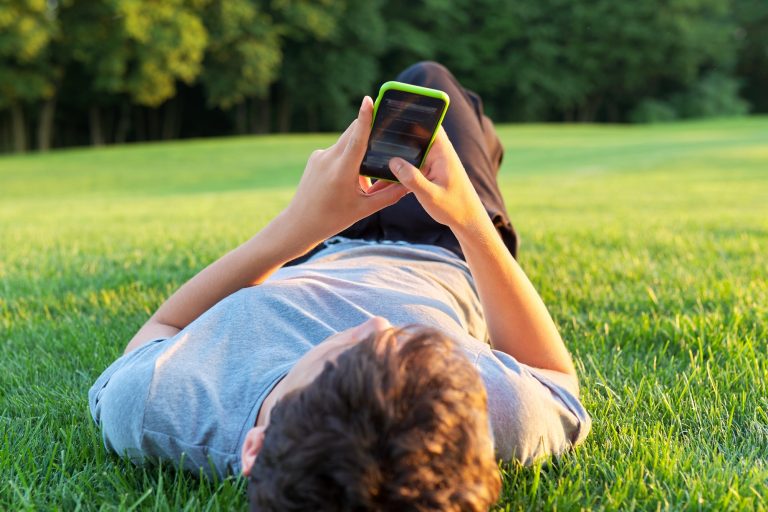 Guy teenager lying on grass with smartphone.