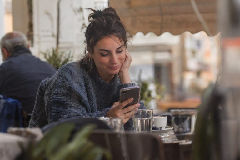 Άτομο με ακουστικά κοιτά την οθόνη κινητού· εικονίδιο φωνητικού μηνύματος και κύματα ήχου συνδέουν το φλερτ με τα ηχητικά μηνύματα.