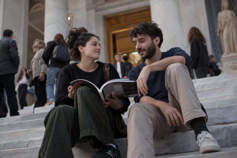 Δύο άτομα σε βιβλιοπωλείο αγγίζουν βιβλία, σχεδιάζοντας ραντεβού σε πολιτιστικό χώρο.
