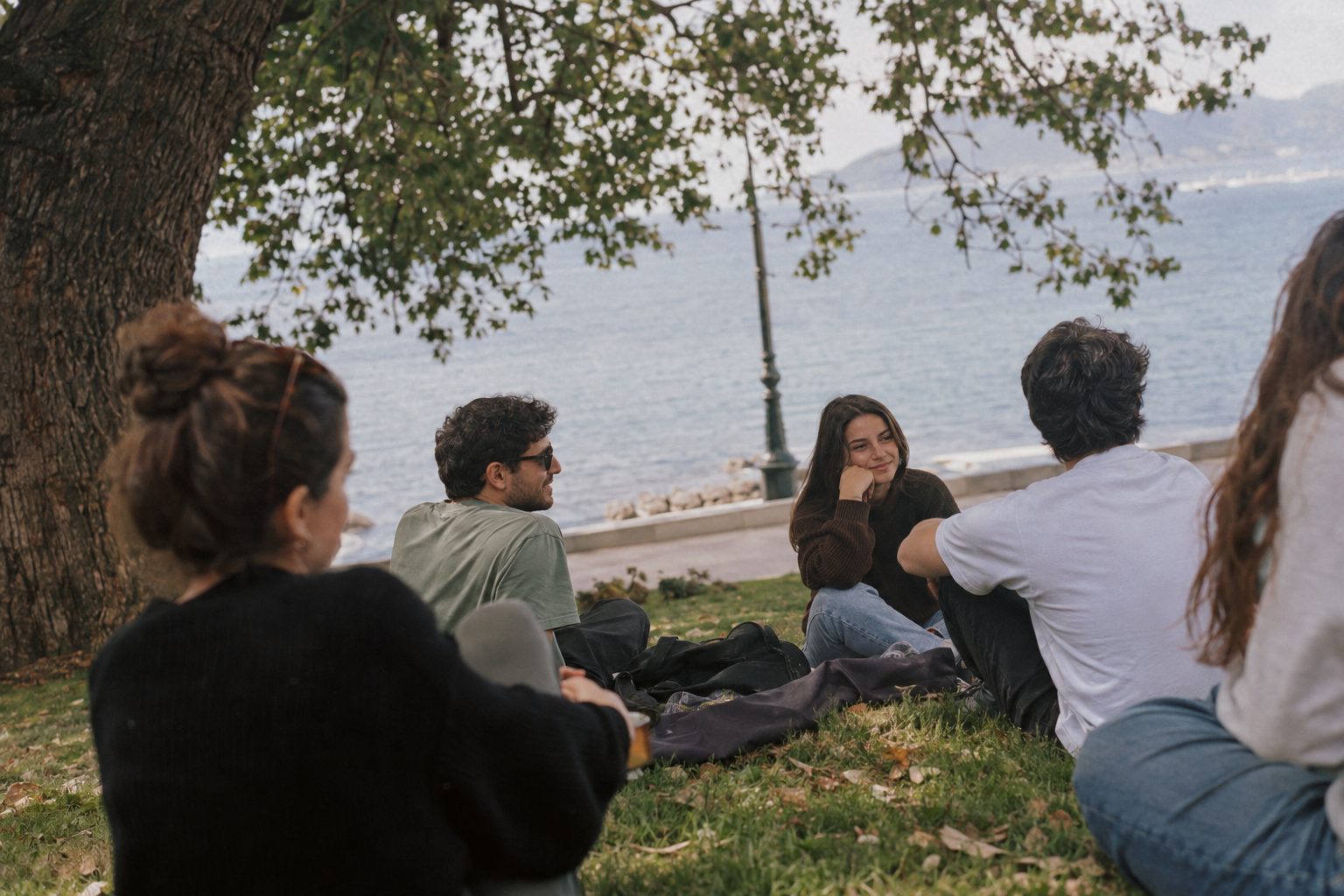 Τραπέζι σε καφέ, δύο άτομα απέναντι, γύρω κοινοί φίλοι συζητούν για τον χωρισμό και τη διαχείρισή του.