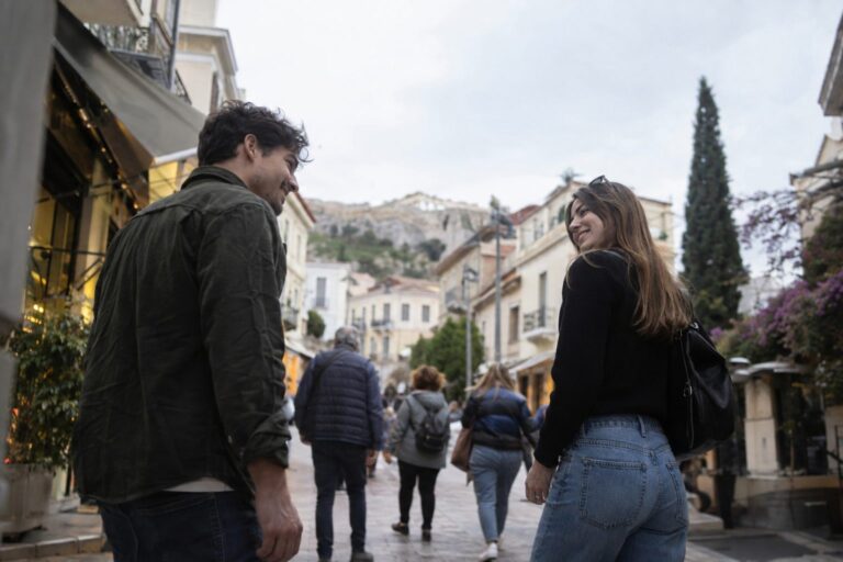 Δύο άτομα σε καφέ χαμογελούν και ανταλλάσσουν βλέμματα, συνδέοντας με ευγενικό φλερτ χωρίς εφαρμογές.