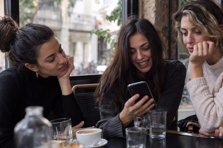 Κοντινό πλάνο smartphone με ανοιχτή ομαδική συνομιλία, εικονίδια προσώπων και συζητήσεις για δεύτερο ραντεβού.