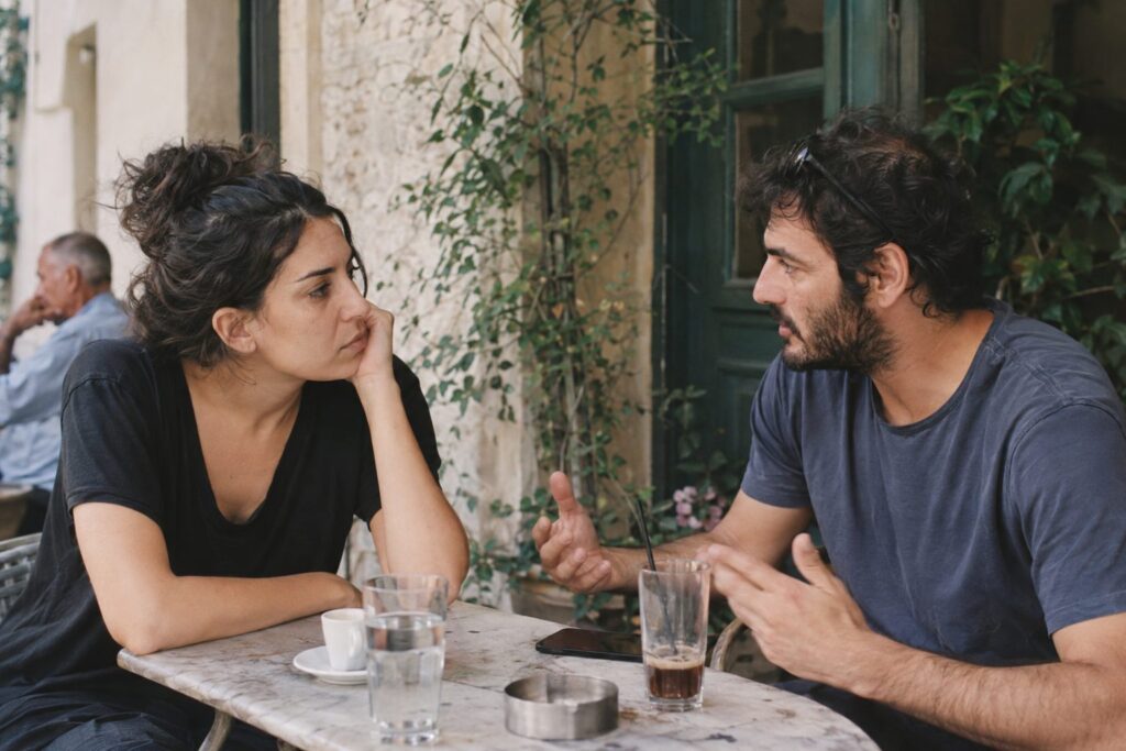 Ζευγάρι σε σχέση κάθεται σε καναπέ, κουβεντιάζει ήρεμα για πολιτικά θέματα, μπροστά τους χαρτιά, δείχνοντας όρια.